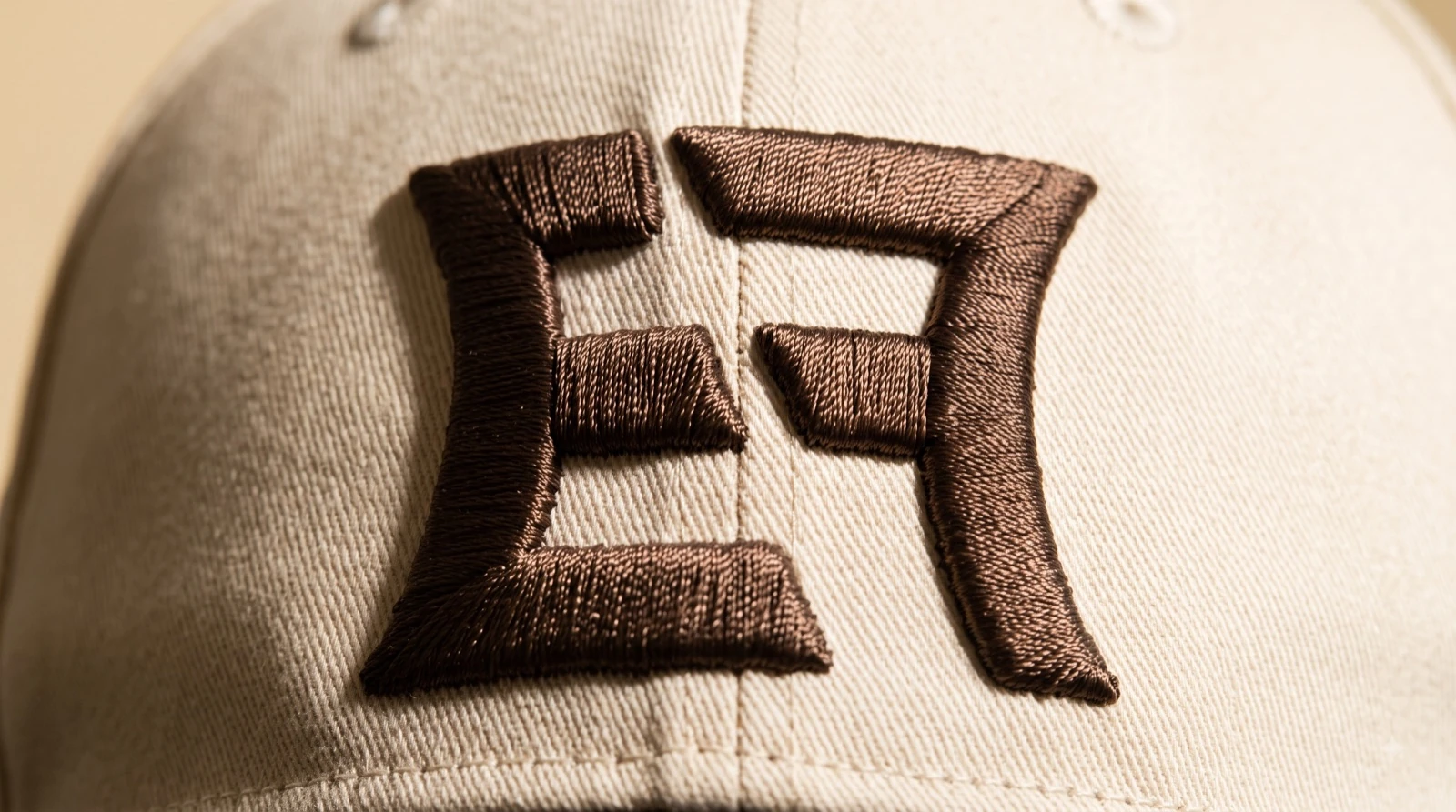 Close-up of the EF monogram embroidered in raised brown satin on off-white cotton twill